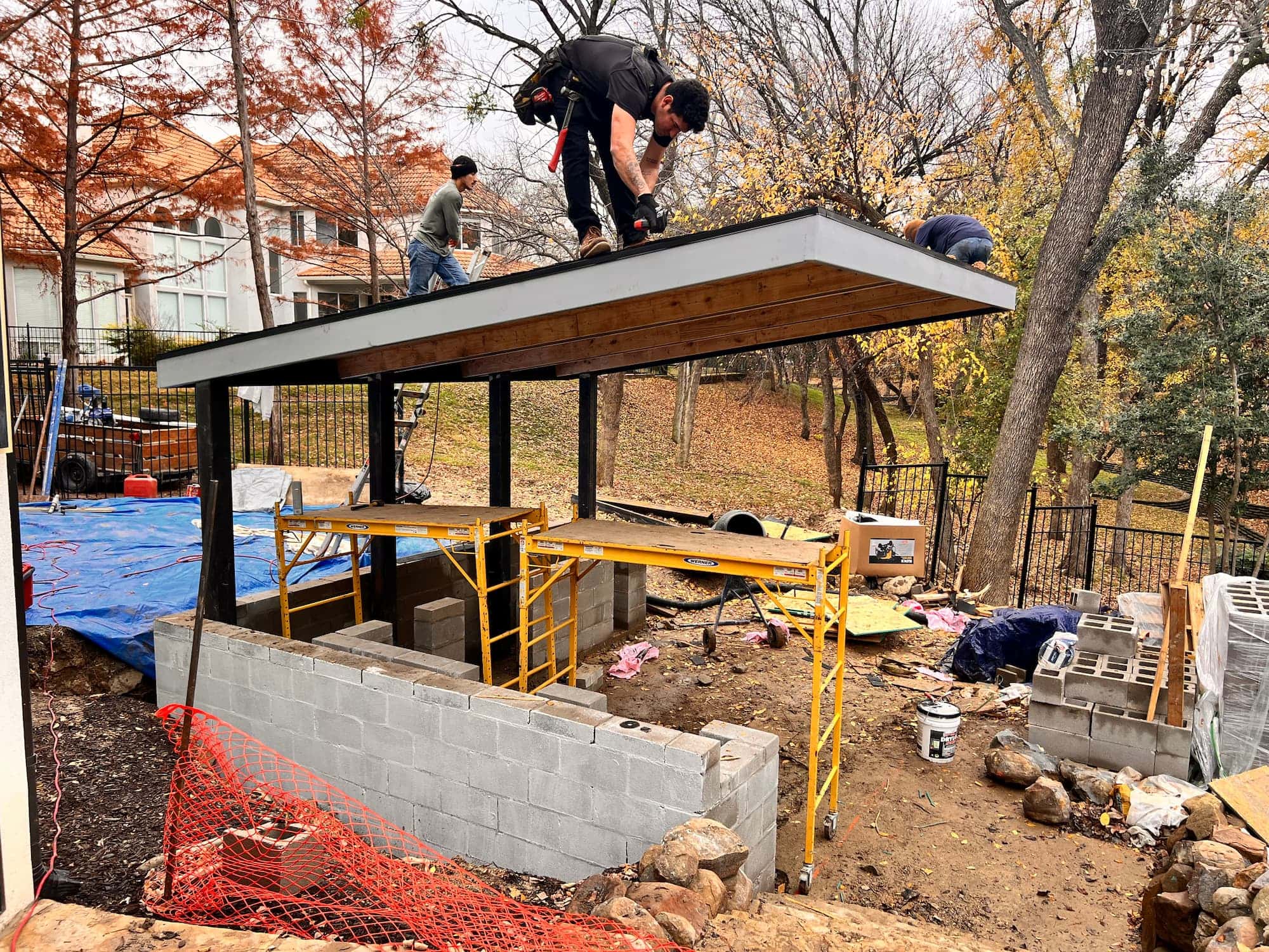 Platinum Pools crew installing an in-house-fabricated cantilevered structural steel roof over a masonry outdoor kitchen during a Stonebriar pool build in Frisco TX
