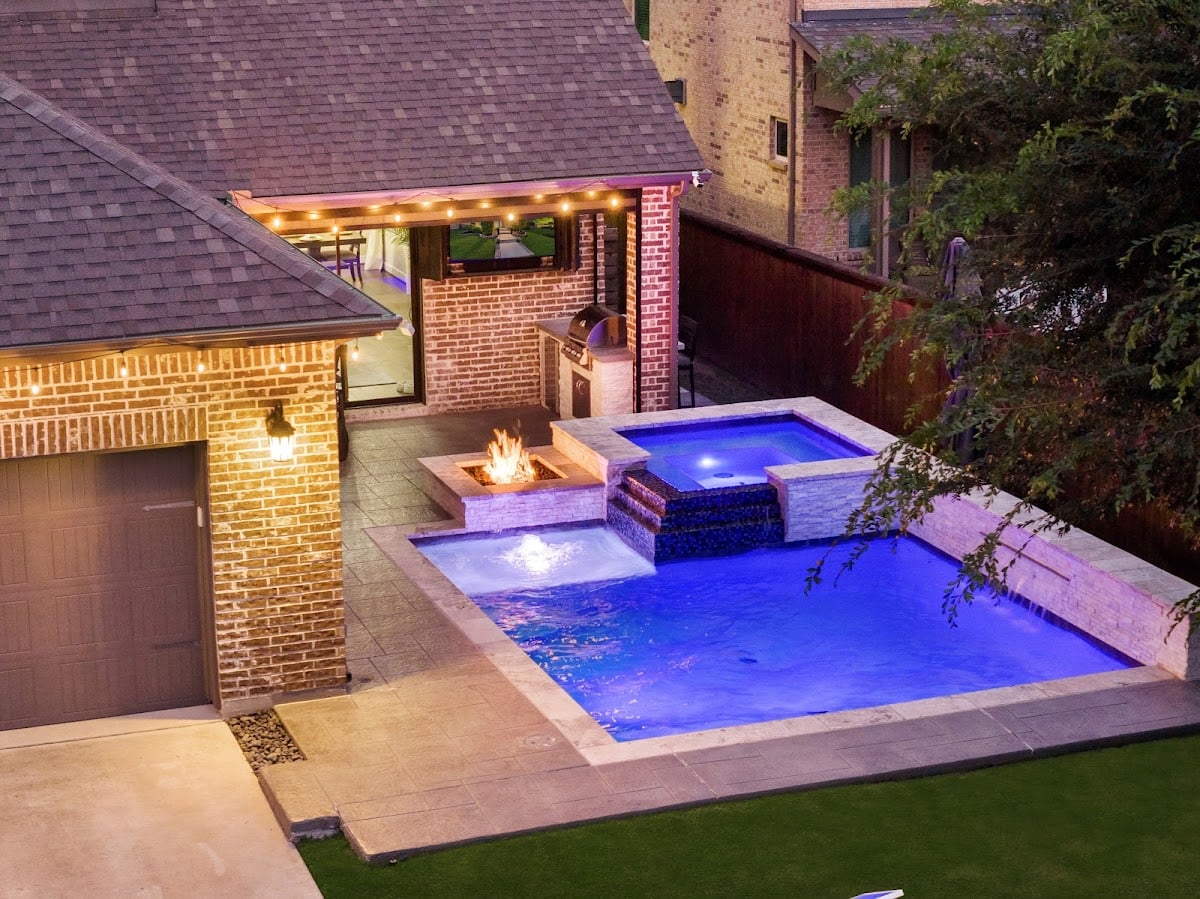 Custom pool with raised spa, fire pit, and outdoor kitchen built by Platinum Pools in Frisco TX